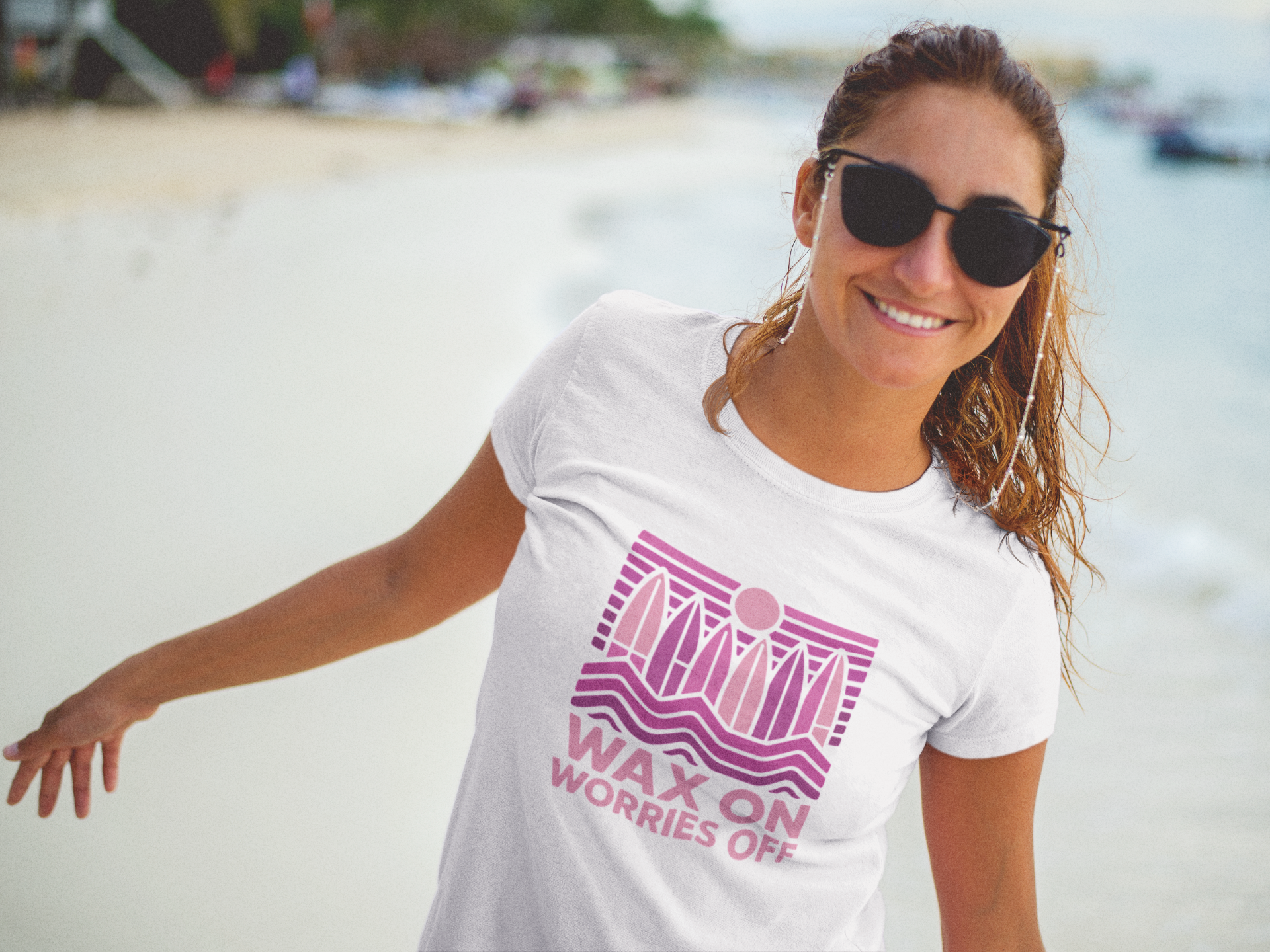 A woman standing on a beach wearing a white t-shirt with a pink graphic that reads 'WAX ON'.